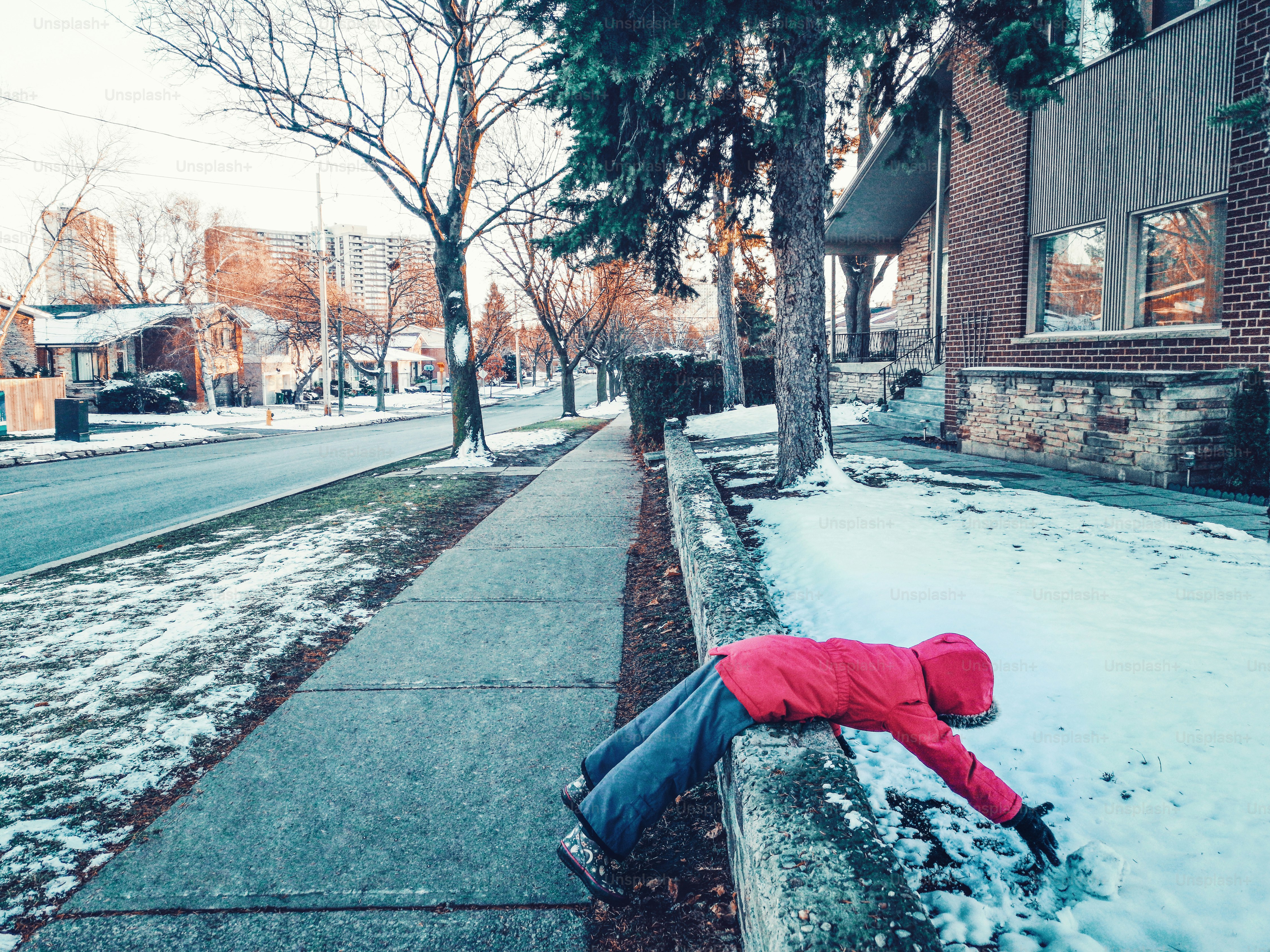 街の通りの雪の中に横たわっている暖かい服のジャケットを着た面白い子供の女の子。寒い冬の日に雪玉作りを楽しんでいる子供。外で遊んでいるいたずらっ子。陽気で面白い奇妙な子供は屋外で。