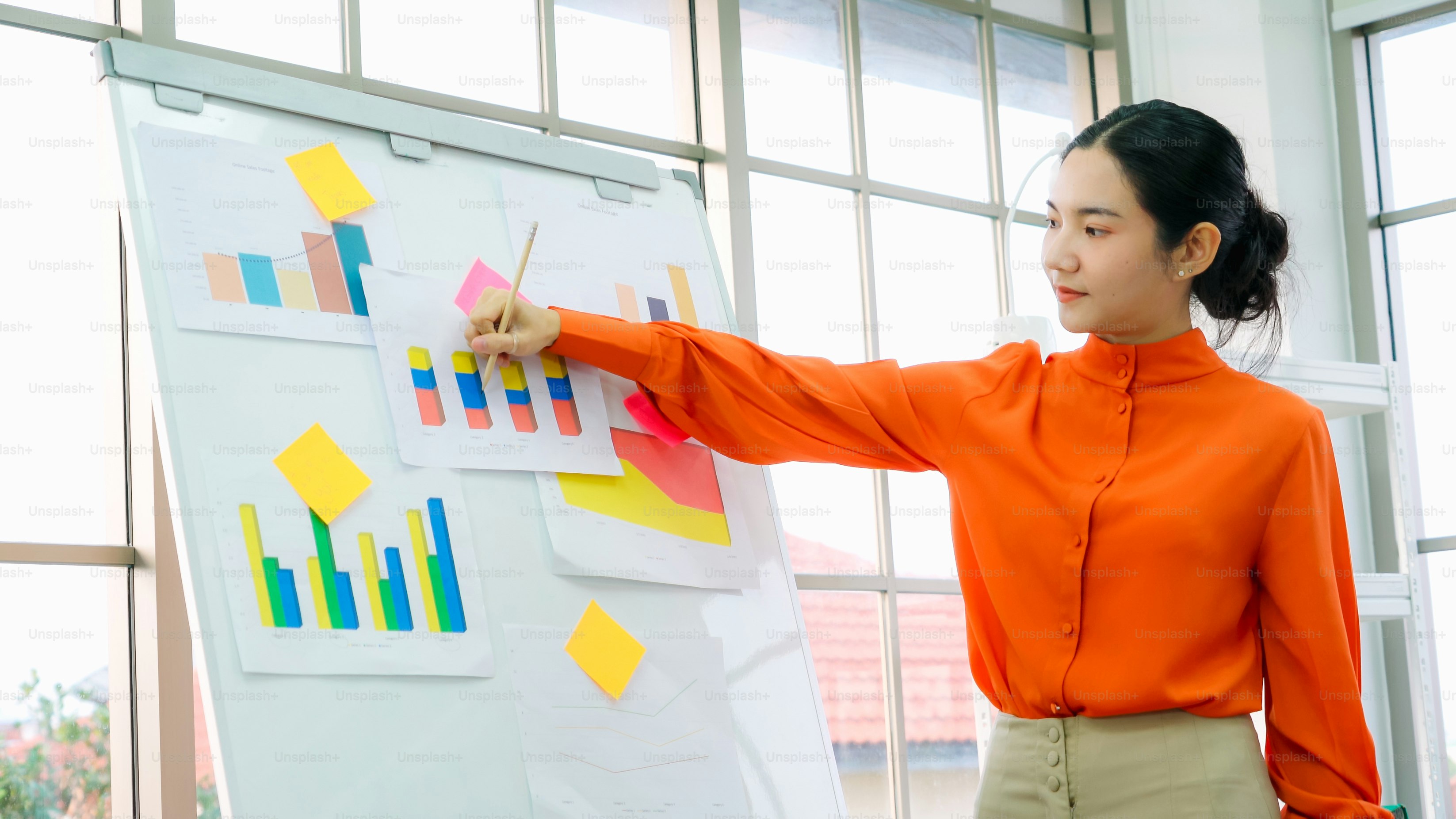Young woman explains business data on white board in casual office room . The confident Asian businesswoman reports information progress of a business project to partner to determine market strategy .