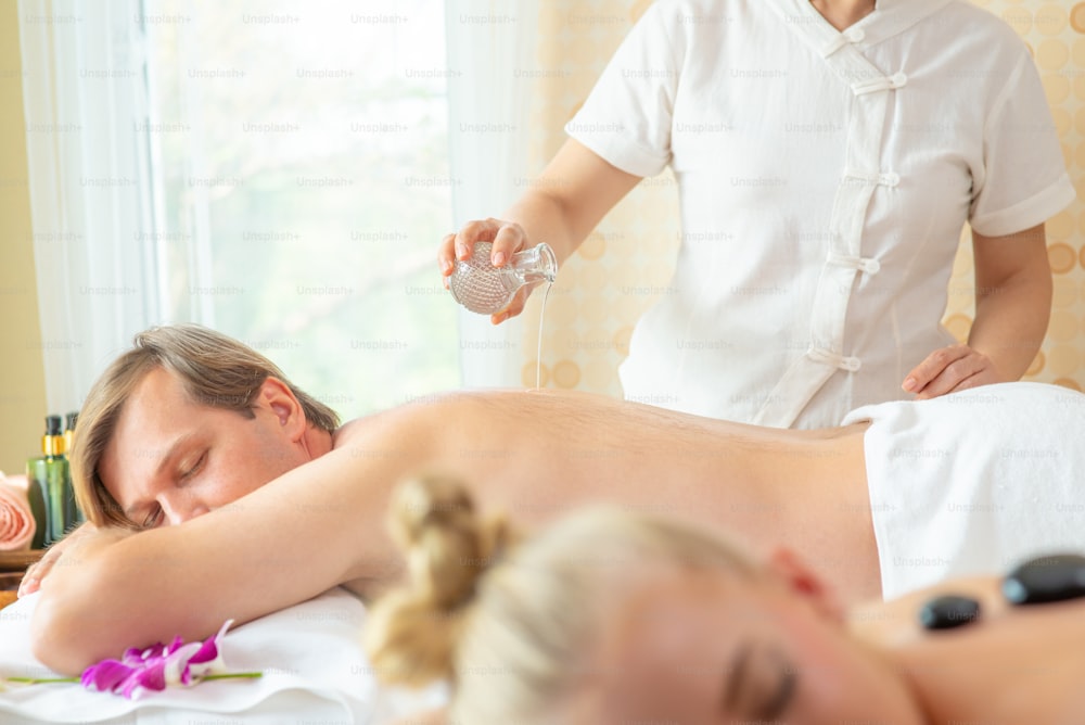 Caucasian man resting on massage bed and get back spa treatment with essential oil from professional therapist at beauty salon