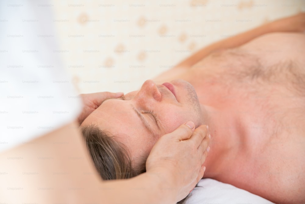 Hombre caucásico descansando en una cama de masaje y recibe un tratamiento de spa facial con aceite esencial de un terapeuta profesional en un salón de belleza