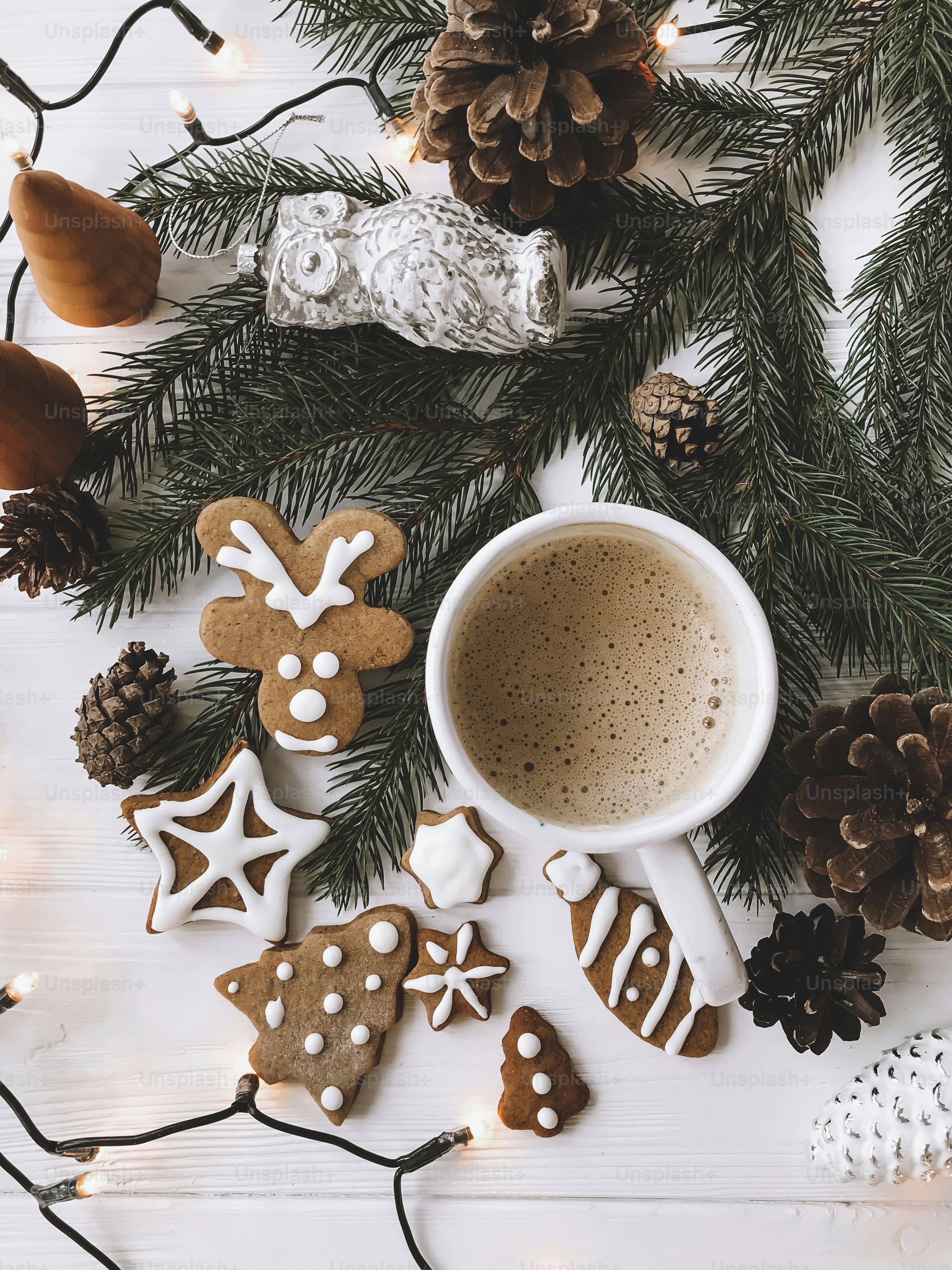 Christmas gingerbread cookies, coffee cup and fir branches on white rustic wooden table with lights. Top view. Happy holidays and Merry Christmas!