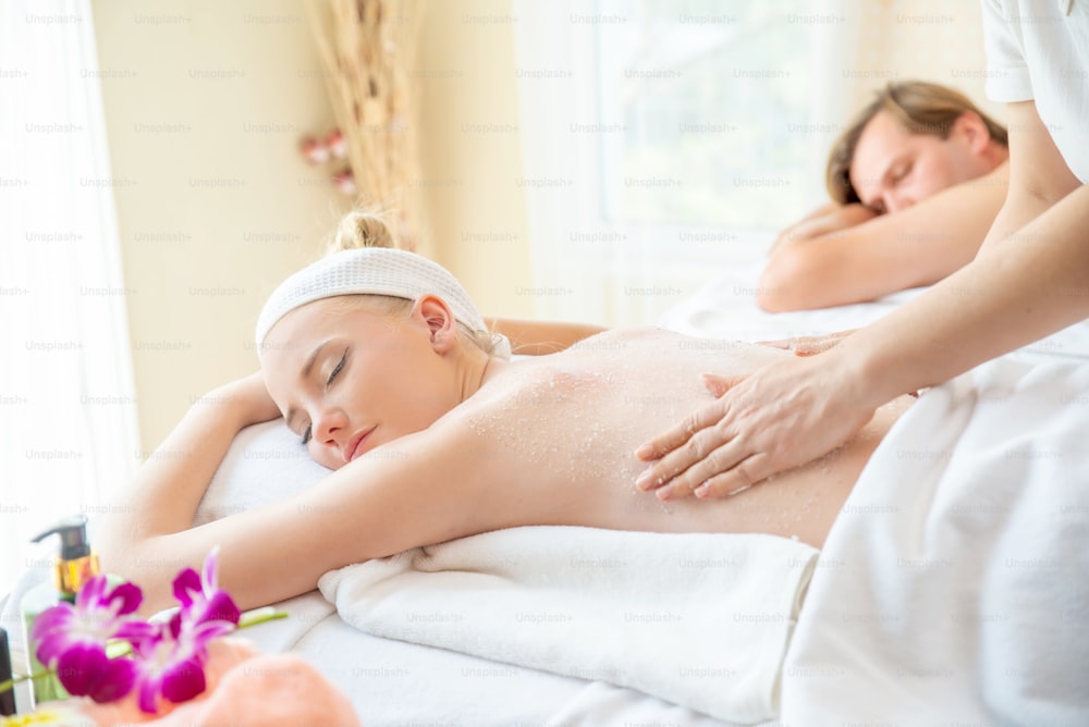 Kaukasische Frau, die auf einem Spa-Bett liegt, bekommt im Schönheitssalon ein Massagepeeling mit Spa-Salz