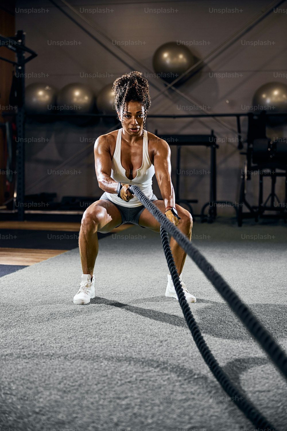 Front view of a strong sporty lady working out with a pair of battle ropes