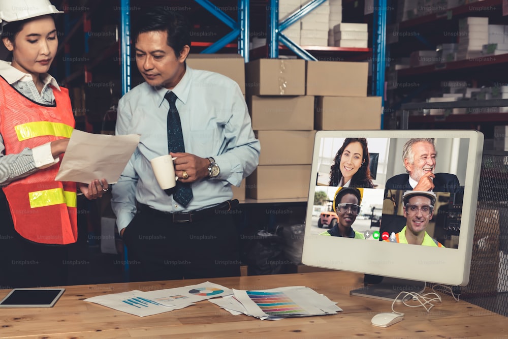 Warehouse staff talking on video call at computer screen in storage warehouse . Online software technology connects people working in logistic factory by virtual conference call on internet network .