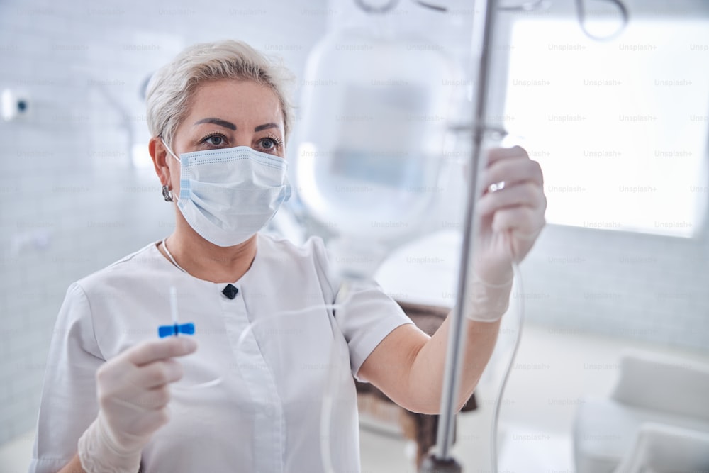 Nahaufnahme Porträt eines erwachsenen kaukasischen blonden Arztes in weißer Uniform mit Blick auf die intravenöse Vitamintherapie in der Medizinklinik
