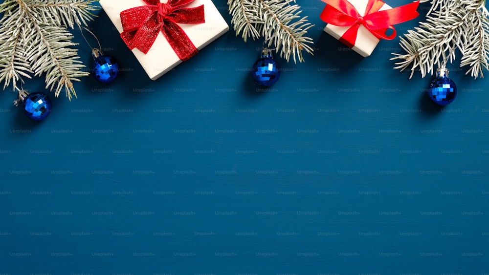 メリークリスマスと新年あけましておめでとうございますグリーティングカードのデザイン。白いギフトボックスで作られたクリスマスフレームの境界線は、赤いリボンの弓、松の木の枝、紺色の背景にボールの装飾を飾りました