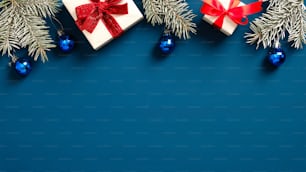 Feliz Natal e Feliz Ano Novo design de cartão de felicitações. Borda do quadro de Natal feita de caixas de presente brancas decoradas laços, galhos de pinheiros, decoração de bolas no fundo azul escuro