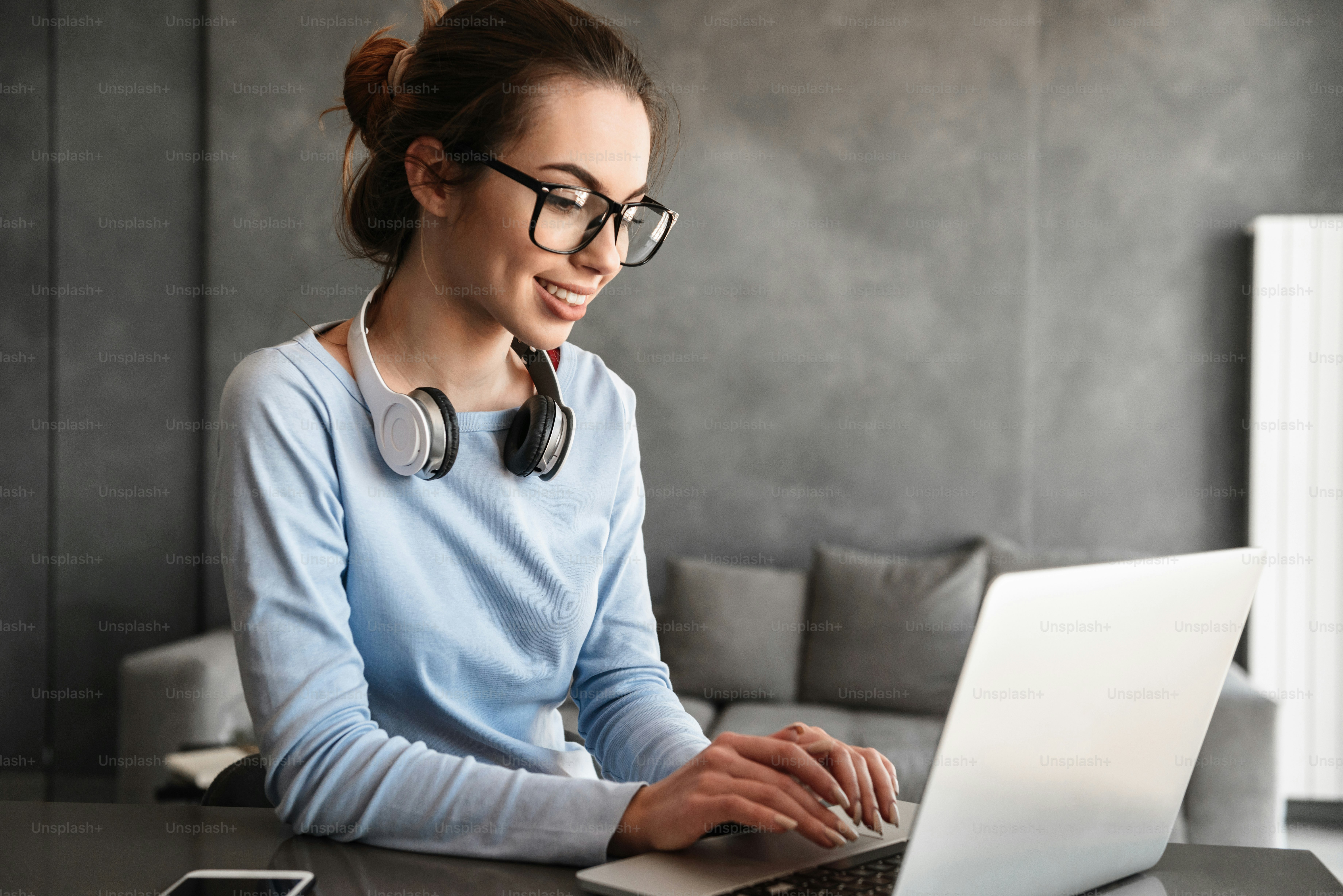 Portrait of an attractive young woman in headphones studying while sitting at the table with laptop computer and notebook at home