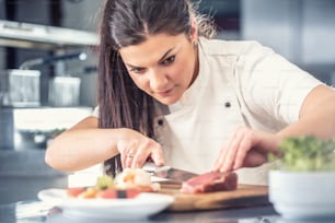 Professional female sushi chef cuts tuna fish in a pro kitchen.