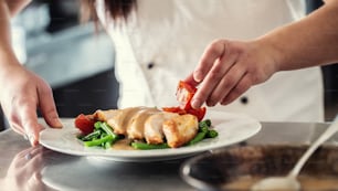 Chef professional in a restaurant prepares food order. Healthy diet in a form of cooked chicken with steamed vegetables.