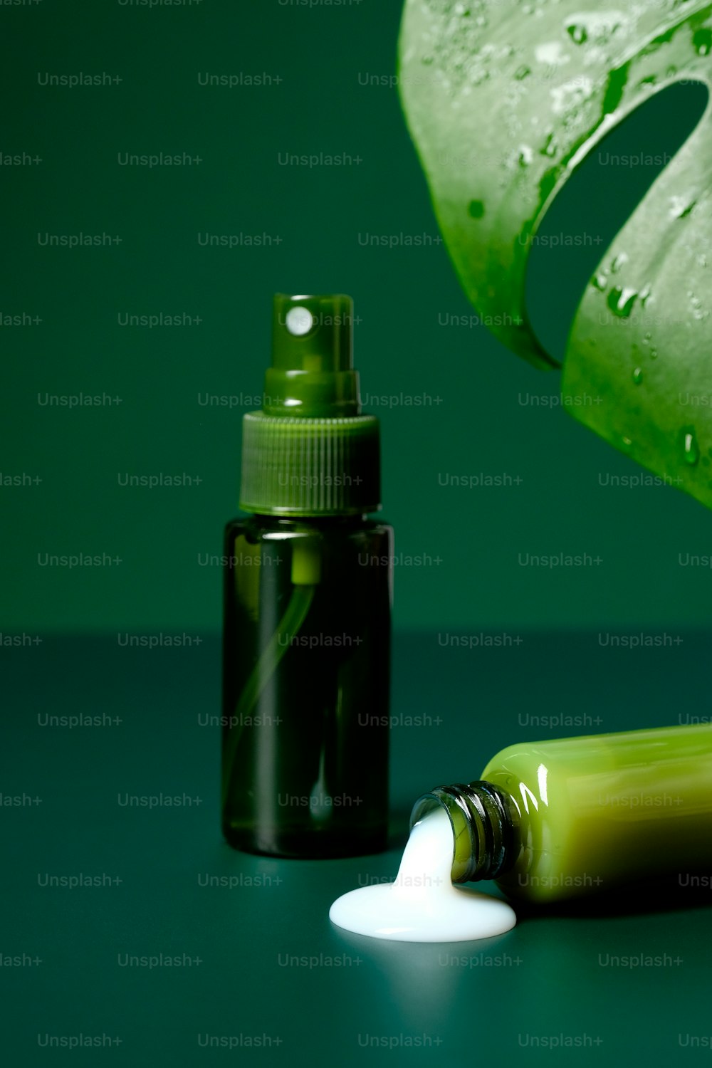Green clear bottles with spray and lotion spilled on table. Natural beauty product. Organic skin care cosmetics set.
