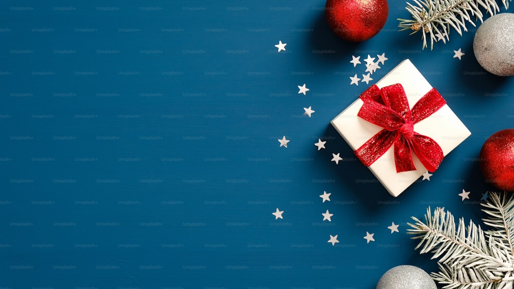 메리 크리스마스와 새해 복 많이 받으세요 선물 상자로 장식된 빨간 리본 활, 진한 파란색 배경에 공이 있는 소나무 가지가 있는 인사말 카드 디자인. 플랫 레이, 평면도, 복사 공간.