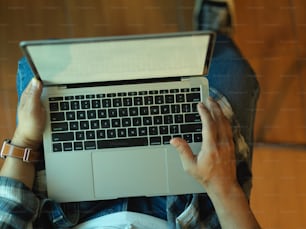 Top view of male hands working with laptop on his lap while sitting in office room
