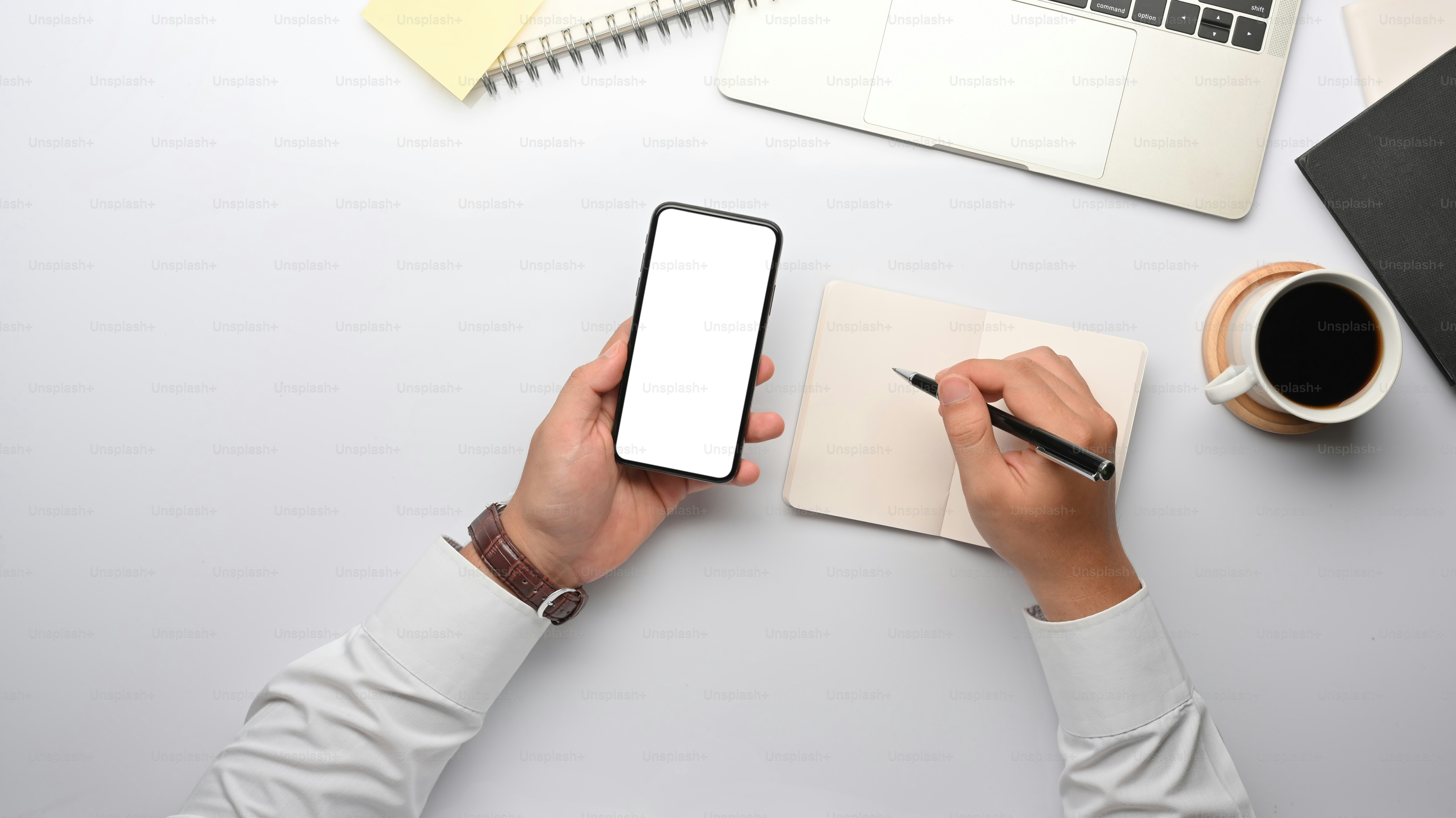 Vista dall'alto dell'uomo d'affari che lavora a mano con lo smartphone e scrive sul taccuino sulla scrivania dell'ufficio