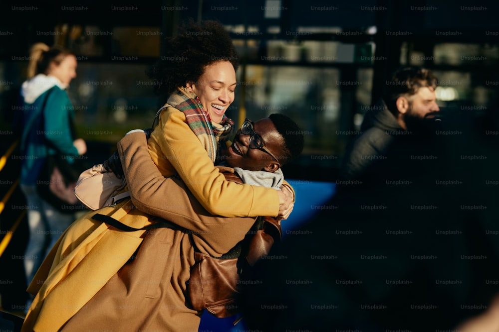 Feliz pareja negra divirtiéndose y abrazándose mientras se reúnen en la estación de autobuses.