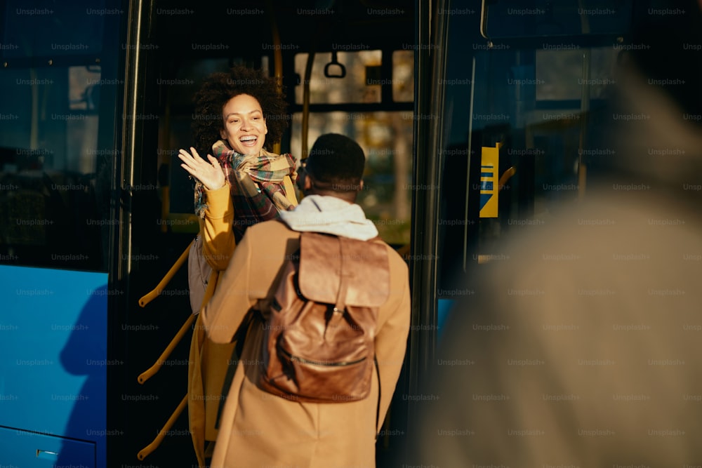 Mulher afro-americana feliz entrando em um ônibus e acenando para seu namorado na estação.
