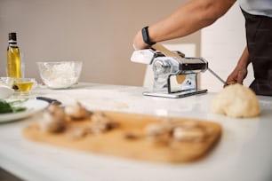 Cropped photo of unrecognized lady using a pasta maker in the kitchen. Website banner