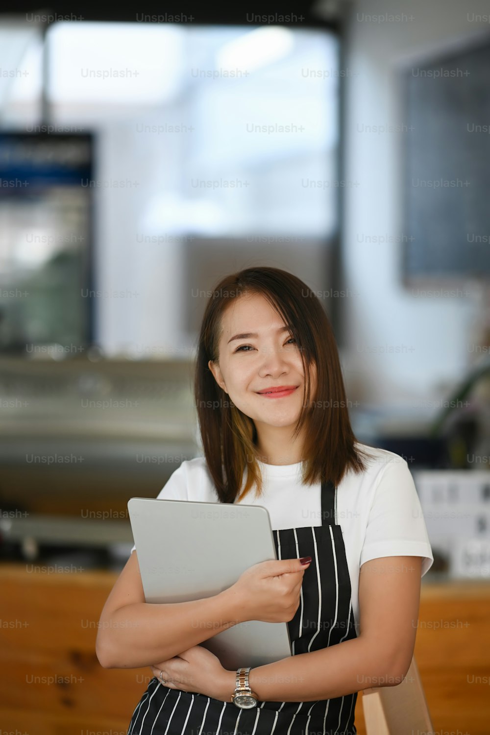 Retrato de una joven empresaria alegre sonriendo y de pie acogedoramente en su moderno café.