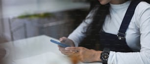 A young female freelancer sitting at her workstation and using smart phone.