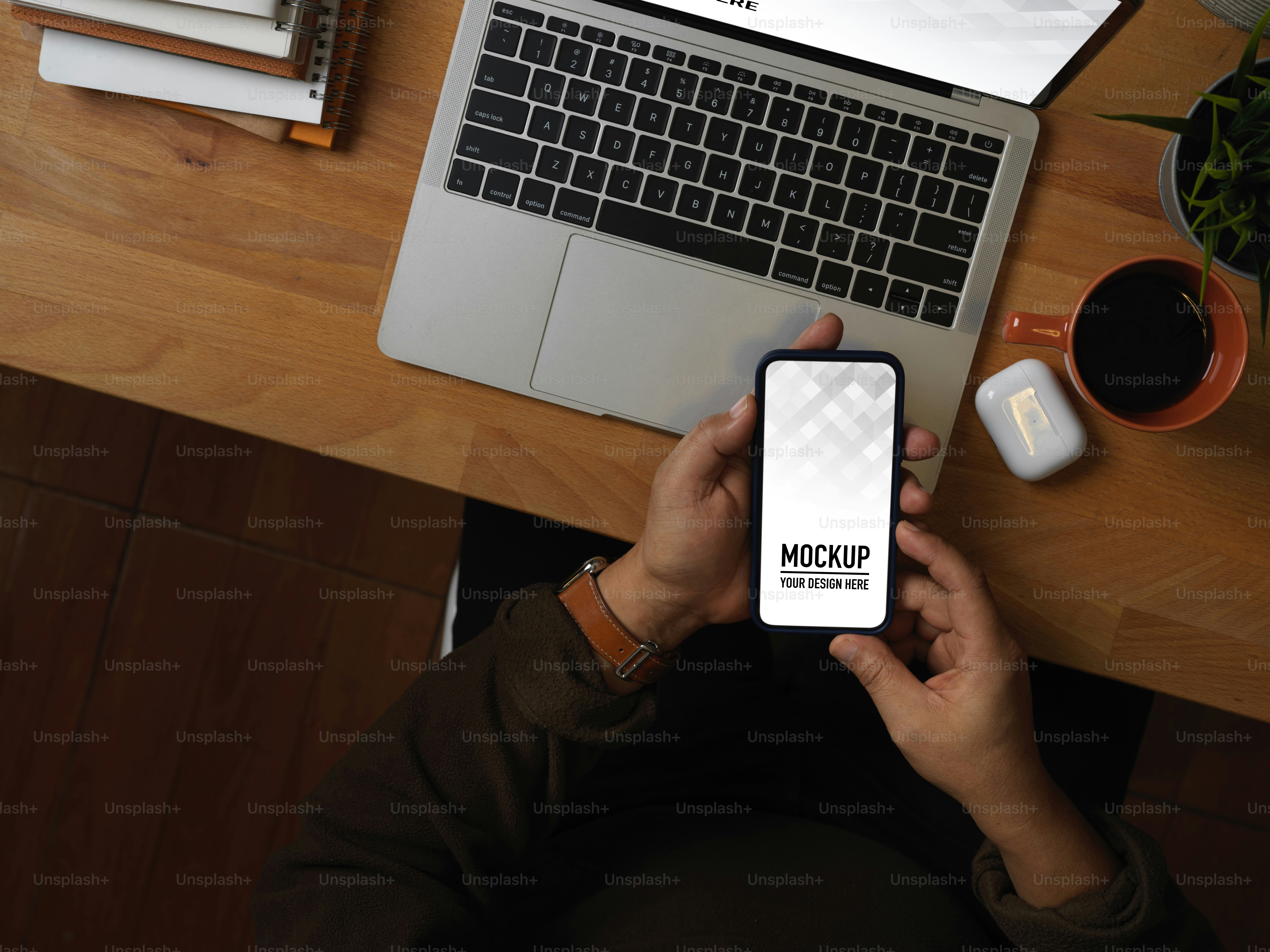 Vista dall'alto della mano maschile che utilizza lo smartphone sul tavolo da lavoro con laptop e forniture