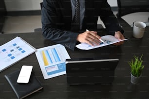 Young successful businessman analyzes financial document ad working with computer tablet in modern office room.