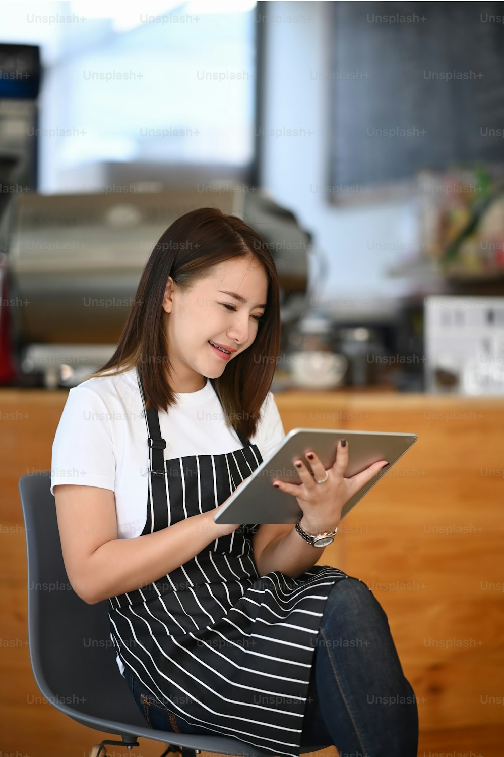 웃고 있는 젊은 기업가가 카페 카운터 앞에 앉아 디지털 태블릿을 사용하고 있다.