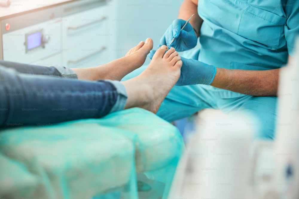 Cropped head portrait of unrecognized doctor un blue uniform and gloves doing pleasant and useful procedure on foot in beauty clinic