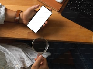 Top view of businessman hand holding smartphone and coffee cup on office table