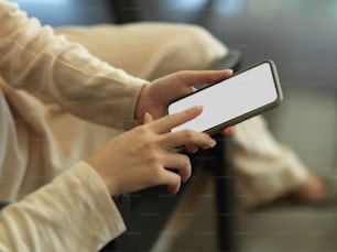 Cropped shot of female touching on smartphone screen while sitting on armchair