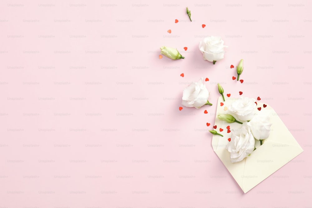 Flowers in envelope and red confetti on pink background. Flat lay, top view, copy space. Love letter, romantic concept. Happy Valentines day greeting card design.