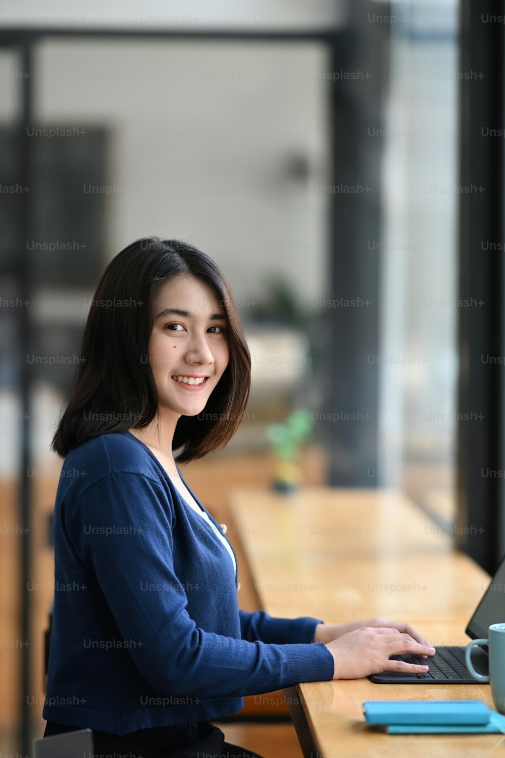 Porträt einer jungen Arbeiterin, die an ihrem Arbeitsplatz sitzt und in die Kamera lächelt.