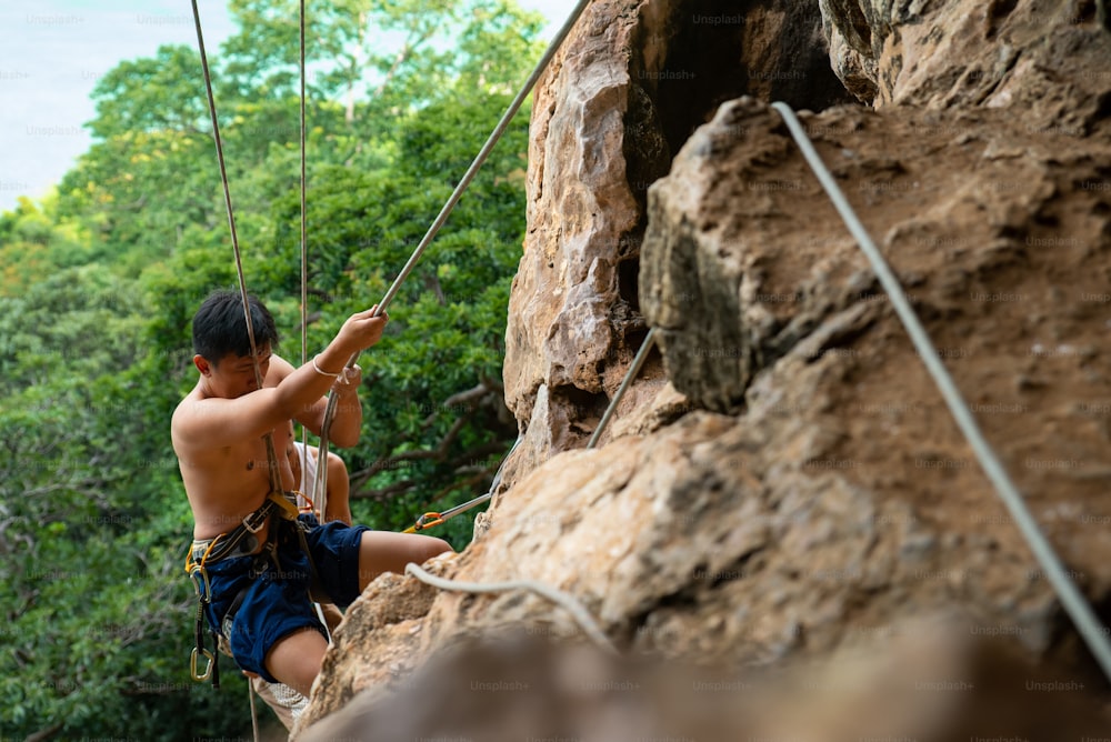Homem asiático descendo na montanha rochosa na ilha tropical no verão.