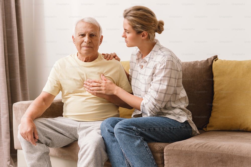 Mujer ansiosa y su padre anciano con una enfermedad coronaria que tienen síntomas de ataque cardíaco en casa