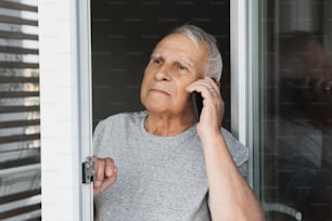Uomo anziano sospetto che guarda nella finestra e fa una chiamata da smartphone