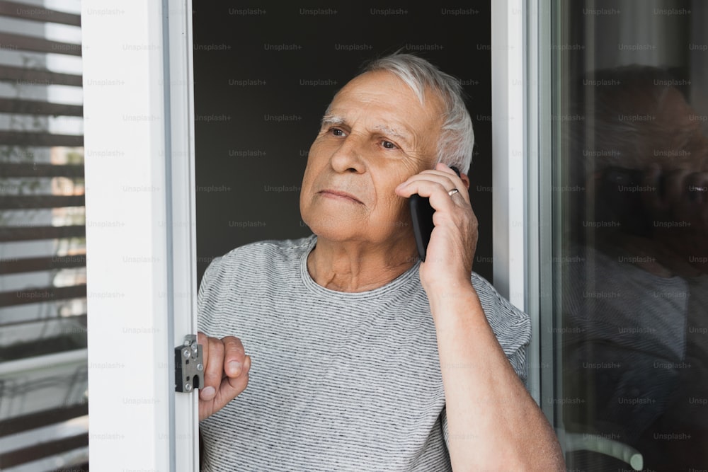 Suspicious elderly man looking into the window and make a call by smartphone