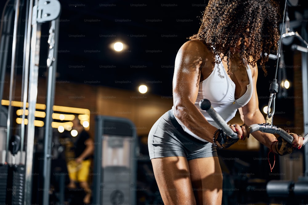 Fitte afroamerikanische Bodybuilderin, die die stehende Trizeps-Pulldown-Übung mit den Fitnessgeräten durchführt