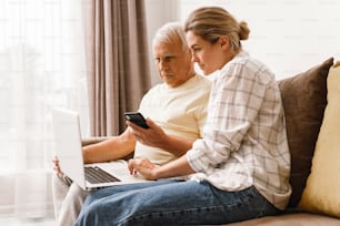 Young woman explaining to elderly man how to use laptop and smatphone