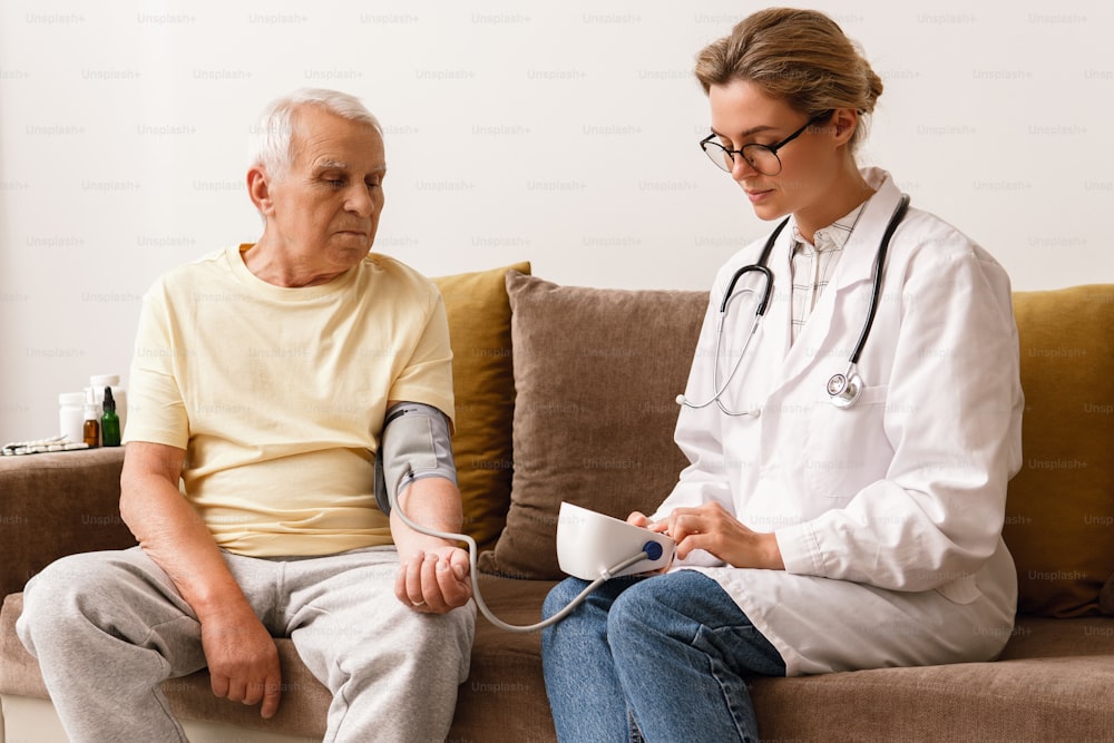 Checking blood pressure. Young woman doctor and elderly man during home visit.