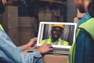 Personnel de l’entrepôt parlant lors d’un appel vidéo à l’écran de l’ordinateur dans l’entrepôt de stockage. La technologie logicielle en ligne connecte les personnes travaillant dans l’usine logistique par conférence téléphonique virtuelle sur le réseau Internet.