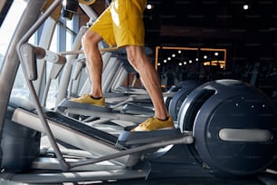 Foto recortada de un hombre caucásico en forma en pantalones cortos haciendo ejercicio en la máquina de cardio