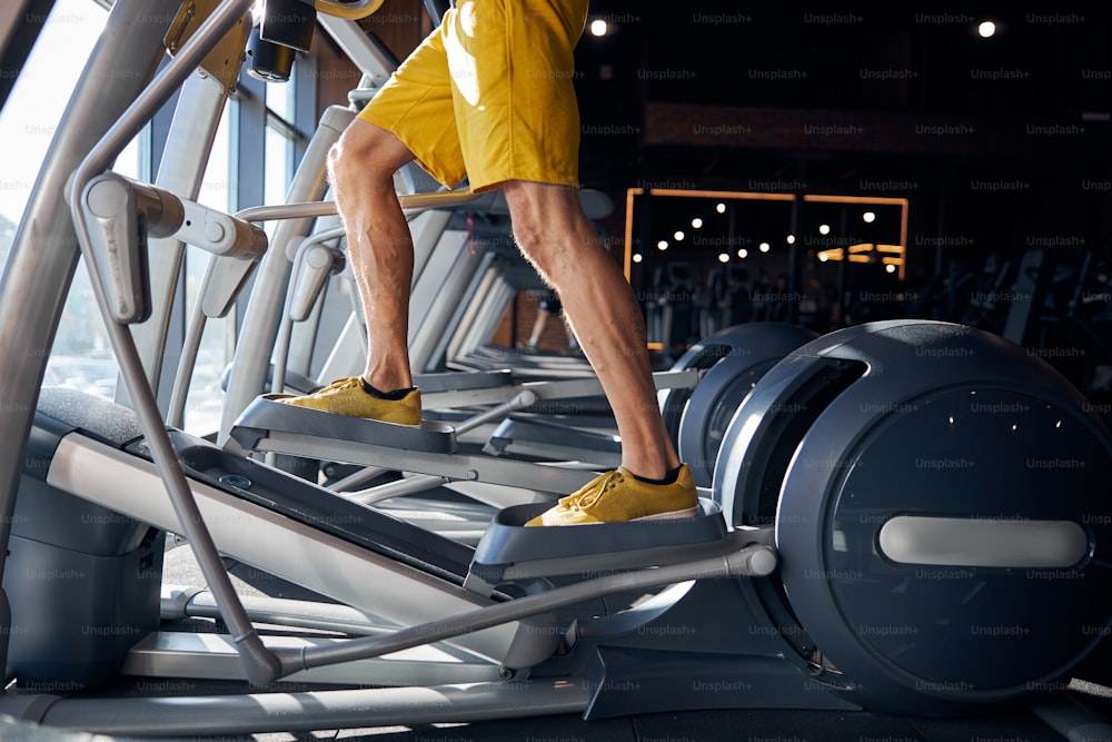 Cropped photo of a fit Caucasian man in shorts working out on the cardio machine