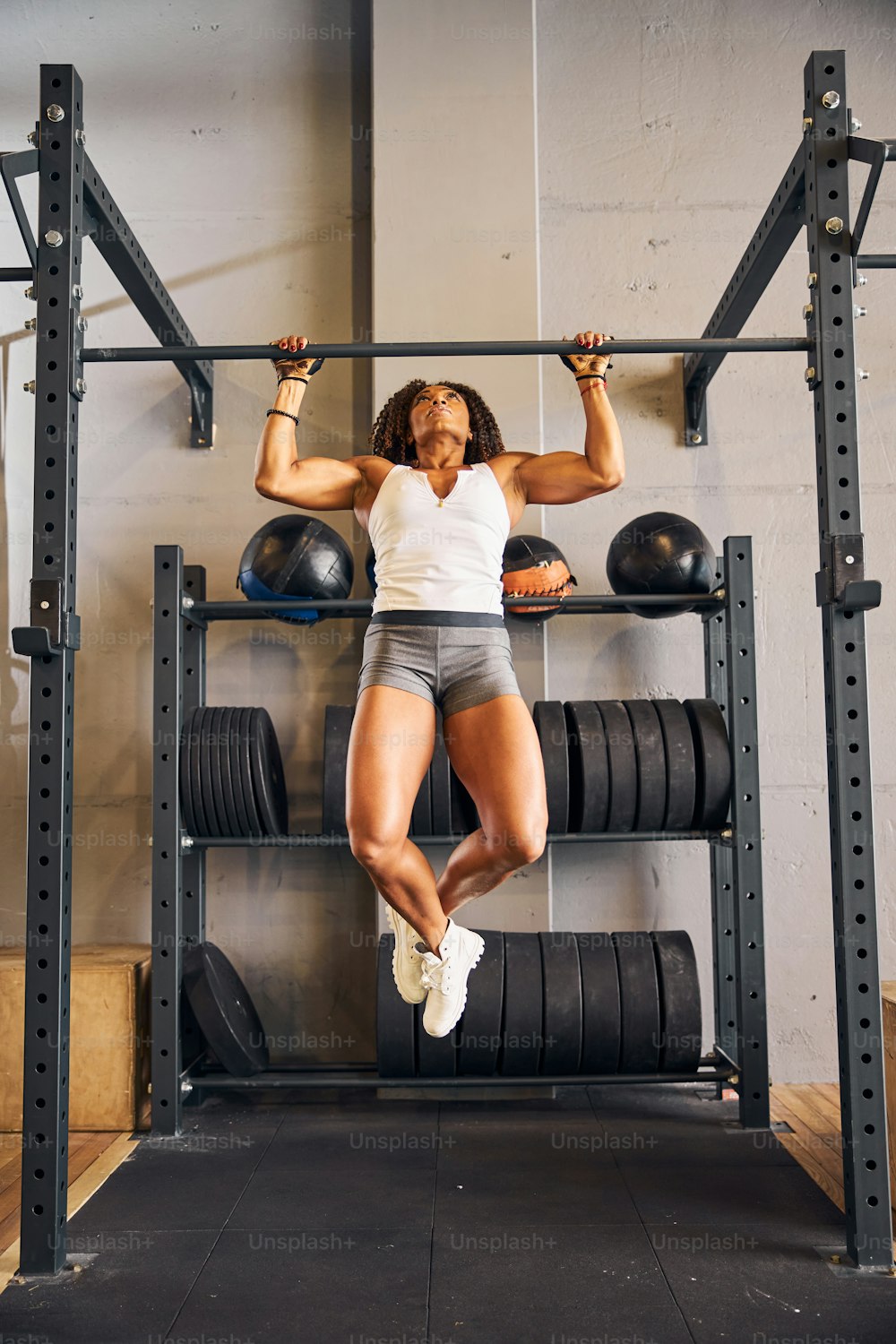 Front view of a sportswoman with her legs crossed performing the pull-up on the horizontal bar