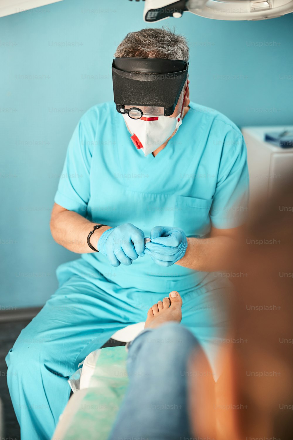 Concentrated podiatrist wearing uniform and mask on face while doing treating procedure