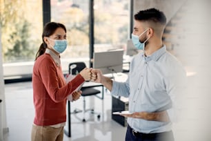Feliz empresaria y su colega chocando los puños mientras saludan en la oficina durante la pandemia de coronavirus. Espacio de copia.