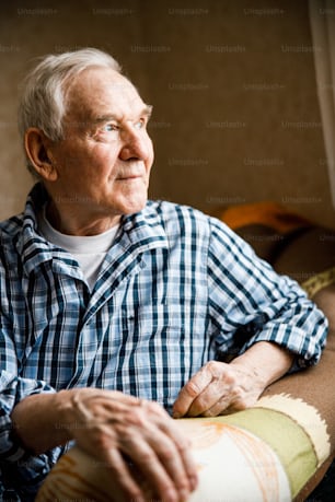 Close-up portrait of happy senior man looking at the window with interest while sitting at the cozy home. Stock photo