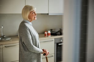 Side view of a smiling pensive female pensioner leaning her hands on the walking stick