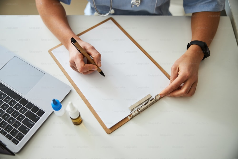 Adult holding a pen over a sheet of paper lying inside a clipboard