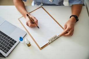 Adult holding a pen over a sheet of paper lying inside a clipboard