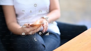 Junge Frau mit Smartphone und Anwendungssymbol auf virtuellem Bildschirm im Büro im Morgenlicht.