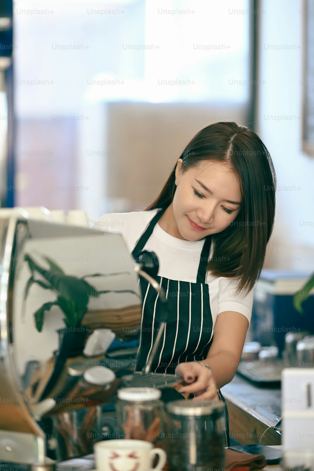 A young woman barista making a cup of coffee while standing behind cafe counter.
